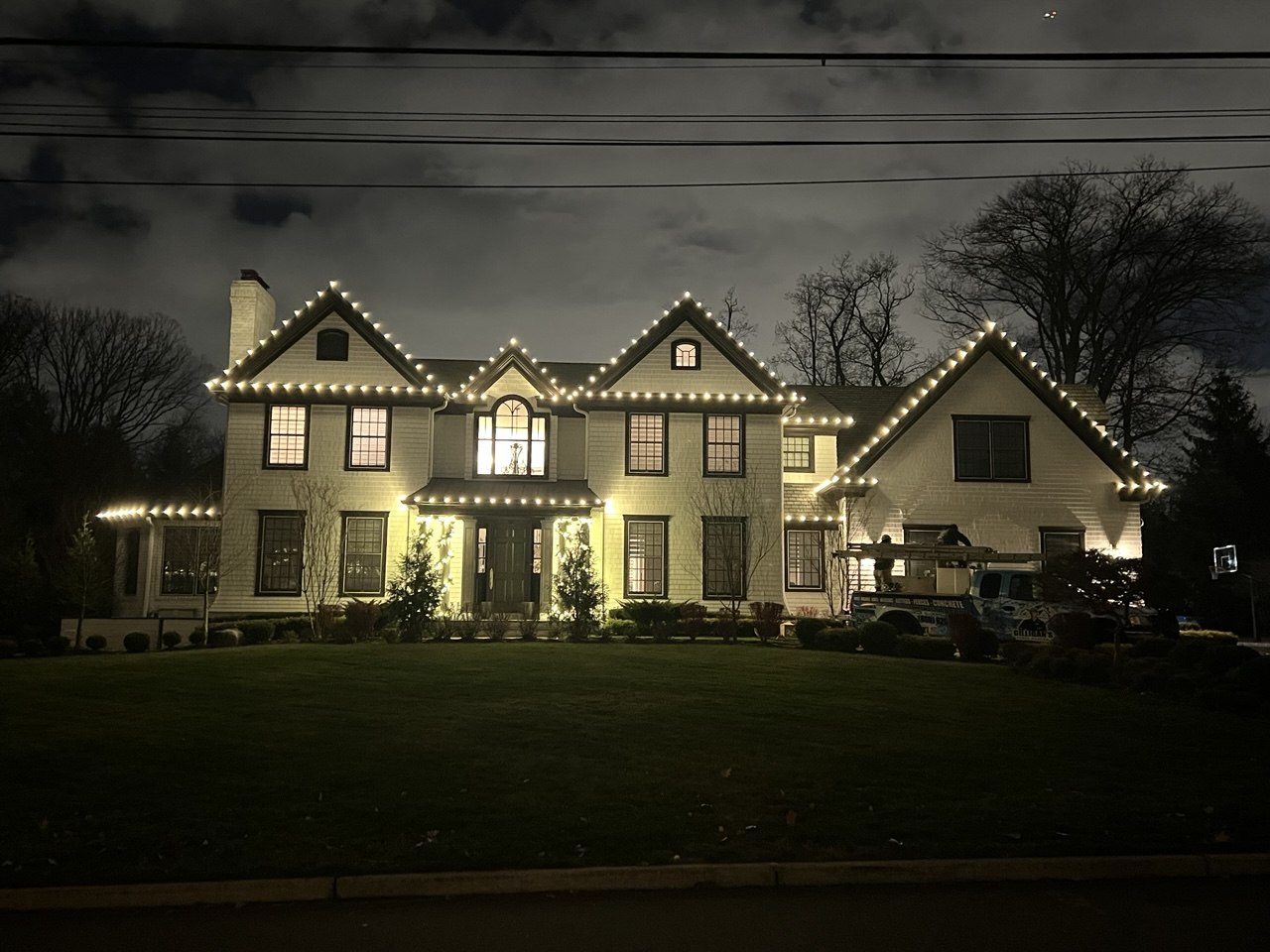 White colonial outlined in warm white lights with the Gilligan's truck