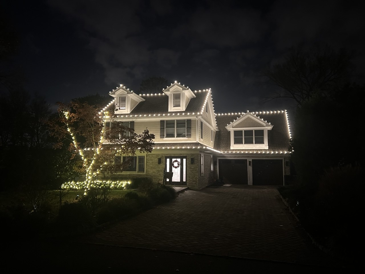 Home with lit dormers and a wrapped tree
